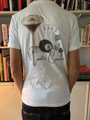 Vit Monte Carlo t-shirt med tryck - Vit t-shirt med coolt Monte Carlo-tryck på ryggen som visar en cocktail, spelkort, biljardboll och tärningar. Klassisk passform med rund hals och korta ärmar. Perfekt för dig som gillar unika motiv och vill sticka ut. Materialet är mjukt och känns som bomull.
