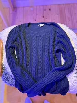Mörkblå kabelstickad tröja H&M - Säljer en mörkblå kabelstickad tröja från H&M BASIC. Tröjan har rund halsringning, långa ärmar och ett klassiskt flätmönster över hela plagget. Perfekt för dig som gillar en enkel men snygg stil.