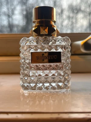 Halv full Valentino parfym med nitar och glas - Säljer en lyxig parfym från Valentino i en transparent glasflaska med coolt nitmönster och guldfärgat lock. Flaskan har en exklusiv känsla med detaljer i guld och en tydlig Valentino-logga på framsidan. Perfekt för dig som gillar snygg design och elegans. Parfymen luktar lyxigt och blommig men inte för söt utan mer fräsch och elegant 