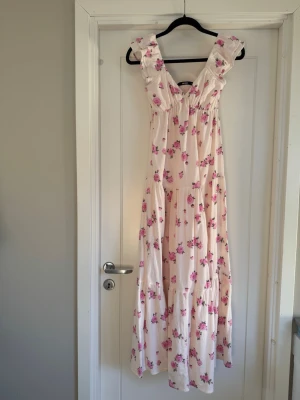 Blommig maxiklänning - BikBok - Romantisk lång klänning från BikBok i ljusrosa med rosa blommor. Klänningen har volangdetaljer vid axlarna och v-ringning. Perfekt för sommardagar och har en luftig, flowy passform. Jag brukar normalt ha small men denna passar small, se sista bilden. Använd vid ett tillfälle 🌸