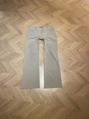 Beige kostymbyxor med smal rand - Snygga beige kostymbyxor med diskreta smala ränder. Byxorna har raka ben och hög midja för en clean och stilren look. Perfekta att matcha med en skjorta eller kavaj för en dressad outfit. De har mini mini ”fläckar” som egentligen inte syns. Mått: midja tvärsöver 41.5cm, innerbenslängd - 79.5cm, benöppning 25cm
