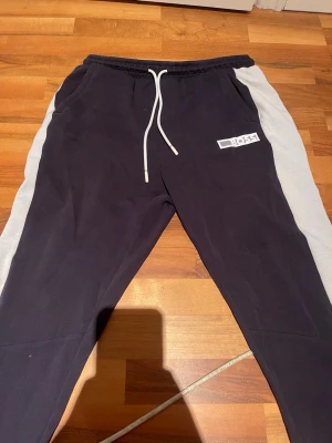 Svarta mjukisbyxor från Boss - Snygga svarta mjukisbyxor från Boss med vita sidopaneler och vit dragsko i midjan. Byxorna har ribbade muddar vid bensluten och Boss-logga på vänster ben. Perfekta för chill eller träning. OBS: Lite slitna