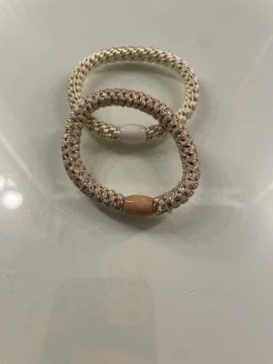 Tofsar  - Säljer två spiralformade hårsnoddar i beige och ljusbrun ton. De är gjorda av elastiskt material med plastdetaljer i mitten, en i vitt och en i ljusbrunt. Perfekta för att hålla håret på plats utan att slita.