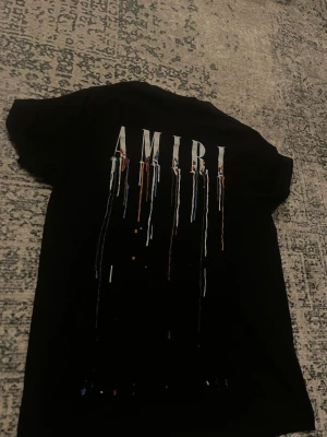  AMIRI t shirt  - Snygg svart t-shirt från AMIRI med unikt drip-print i vitt, blått och orange både fram och bak. T-shirten har korta ärmar och klassisk passform. Perfekt för dig som gillar streetwear och vill sticka ut med cool design. Passar både M och S 
