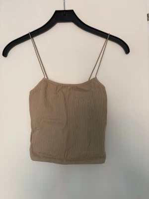 Beige ribbad linnetopp från Zara - Snygg beige ribbad linnetopp från Zara med smala axelband och croppad passform. Perfekt att styla med jeans eller kjol för en trendig look. Enkel och stilren design som passar till många outfits.
