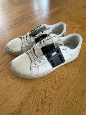 Vita sneakers från 11 by Boris Bidjan - Säljer ett par vita sneakers från 11 by Boris Bidjan Saberi med svarta detaljer i plast över snörningen. Skorna har en chunky sula, klassisk låg profil och är tillverkade i läder med textilfoder. Snygg kontrast mellan vitt och svart gör dem riktigt unika.