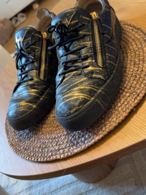 Giuseppe Zanotti skor - Äkta Limited Edition Giuseppe Zanotti May London sneakers i svart läder med guldfärgat mönster och karakteristiska guldfärgade dragkedjor.