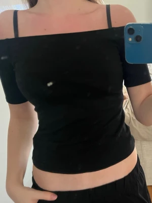 Svart offshoulder topp - Trendig svart offshoulder topp med korta ärmar och croppad passform. Perfekt till höga jeans eller kjol för en snygg och enkel look. Tunn och mjuk i materialet, passar till många olika stilar.
