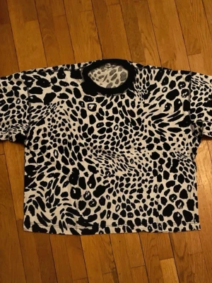 Svartvit leopardmönstrad t-shirt - Cool svartvit t-shirt med leopardmönster och svart ribbad krage. Oversized passform och korta ärmar ger en avslappnad vibe. Perfekt för dig som vill sticka ut med ett djuriskt tryck.💕💕