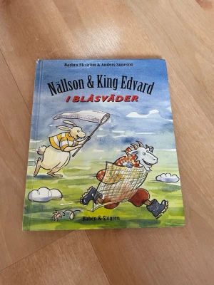 Nällson & King Edvard i blåsväder - En färgglad bilderbok med titeln 'Nällson & King Edvard i blåsväder' av Barbro Ekström och Anders Suneson. Omslaget visar två tecknade djurfigurer i fartfylld miljö. Boken har hårt omslag och är rikt illustrerad, perfekt för unga läsare.