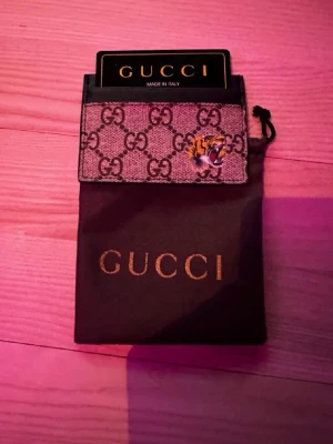 Gucci korthållare med tigerdetalj - Säljer en snygg korthållare från Gucci i beige/brunt canvasmaterial med klassiskt GG-mönster och en broderad tigerdetalj. Kommer med originalpåse. Perfekt för kort och ID, stilren och lyxig design.