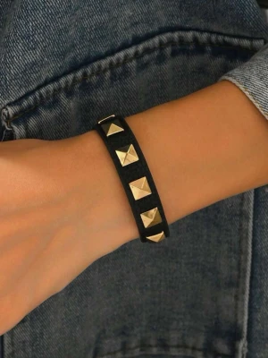 Svart armband med guldfärgade nitar - Snyggt svart armband i konstläder med fyrkantiga guldfärgade nitar längs hela bandet. Armbandet har tryckknappsstängning och en stilren, edgy look som passar perfekt till jeansjacka eller skinnjacka.