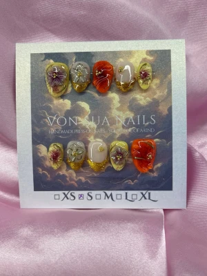 Aurelia (S);Short Almond - Unika handgjorda press-on naglar med handskulpturerade 3D blommor i lila och guld, samt accentnaglar i orange och gult. Naglarna har en kort mandel form och dekoreras med gulddetaljer och små pärlor för en lyxig känsla. Perfekt för dig som vill sticka ut med din nagelstil.S: 15 mm, 11,5 mm, 12 mm, 11 mm, 9 mm 