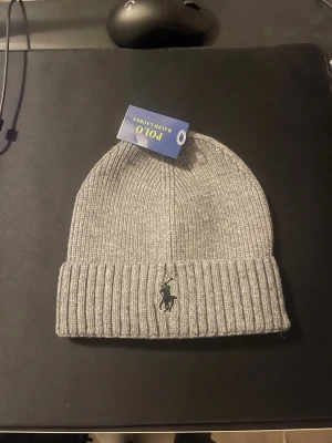 Ralph Lauren - Grå ribbstickad mössa från Polo Ralph Lauren. Helt oanvänd. Perfekt under kalla dagar.