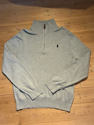 Grå halvzip tröja från Polo Ralph Lauren - Tyvärr har lappen i nacken gått sönder men annars Snygg grå långärmad tröja från Polo Ralph Lauren med halvzip och hög krage. Tröjan har det klassiska broderade logotypen på bröstet och är tillverkad i mjukt material. Perfekt för lager-på-lager och chill stil.