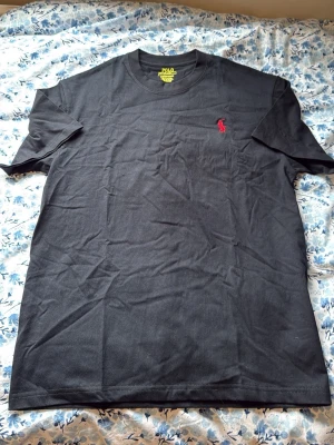 Svart t-shirt från Polo Ralph Lauren - svart t-shirt från Polo Ralph Lauren med röd broderad logga på bröstet. Perfekt basplagg med stilren design. Helt ny aldrig använd storlek M 