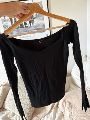 Svart långärmad topp med v-ringning  - Säljer en svart långärmad topp med v-ringning och offshoulder-design. Toppen är tight i modellen med utsvängda armar.Tillverkad i mjukt bomullsmaterial för en bekväm känsla. Den är från Gina Tricot och använd fåtal gånger. Lappen är bortklipp då den stack i ryggen, men detta är inget som synd eller känns på. 