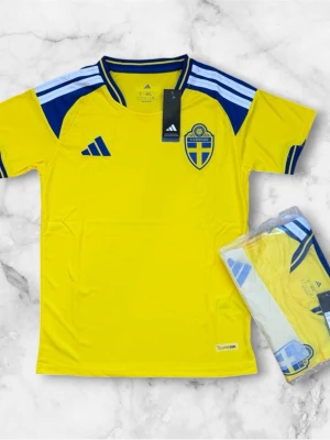 Svensk landslagströja Adidas gul/blå - Säljer en officiell svensk landslagströja från Adidas i gult med blå detaljer och vita ränder på axlarna. Tröjan har Sveriges landslagsemblem på bröstet och klassisk sportig design. Tillverkad i lätt och ventilerande material, perfekt för fotboll eller träning.