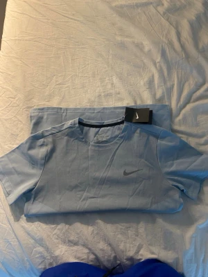 Ljusblå Nike t-shirt - Snygg ljusblå t-shirt från Nike med klassisk logga på bröstet. Tillverkad i ett lätt och bekvämt material som passar perfekt till träning eller chill. T-shirten har rund halsringning och korta ärmar för en clean och sportig look.