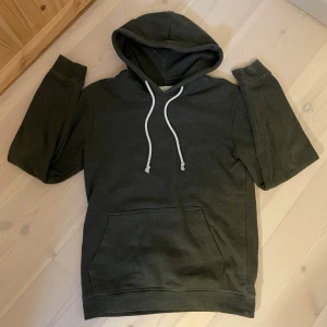 HOODIE | PIER ONE. - En stilren mörkgrön hoodie med klassisk känguruficka och vita dragsnören i huvan. Hoodien har en avslappnad passform och ribbade muddar vid ärmar och nederkant. Perfekt för en chill och casual look.