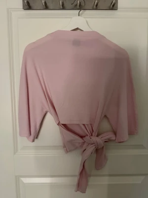 Ljusrosa omlottopp med knyt - Supersöt ljusrosa omlottopp med knyt i midjan och trekvartsärm. Perfekt för dig som gillar en feminin och avslappnad stil. Tunn och mjuk, passar till många olika outfits.