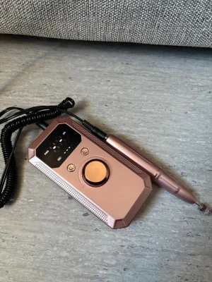 Elektrisk nagelfil med tillbehör - Säljer en elektrisk nagelfil i roséguld med digital display och kontrollratt. Medföljer flera sliphuvuden och sliprullar i olika material och former, perfekt för manikyr och pedikyr. Smidig design och enkel att använda för både nybörjare och proffs.