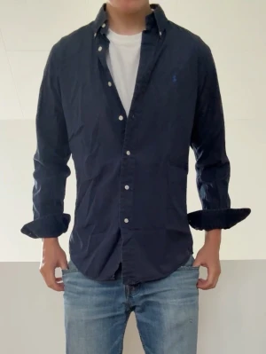 Mörkblå Ralph Lauren skjorta - Mörkblå Ralph Lauren skjorta i strl M men sitter som en S! Bra skick utan nåra defekter och hör gärna av er vid frågor elr funderingar!!