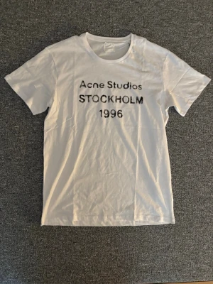 Vit Acne Studios t-shirt Stockholm - Säljer en vit t-shirt från Acne Studios med trycket 'Acne Studios STOCKHOLM 1996' på bröstet. Klassisk rund hals och korta ärmar. Perfekt basic-plagg med clean design och skön passform. ALLA lappar saknas därav priset