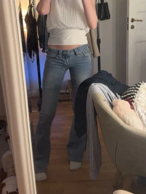 Ljusblå bootcut jeans från True Religion - Säljer ett par ljusblå bootcut jeans från True Religion med låg midja och klassiska kontrastsömmar. Jeansen har fickor med lock och knapp bak samt en tydlig logopatch i bak. Perfekta för dig som gillar retrovibbar och snygg passform. Perfekta till fester å även dagligt bruk 