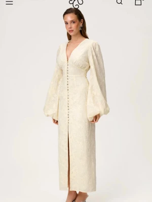 Ljus gul  spetsklänning från Adoore - Superfin ljus  gul spetsklänning från Adoore med v-ringning, långa puffärmar och knappar framtill. Klänningen har vackra broderade blommor i tyget och en feminin siluett. 