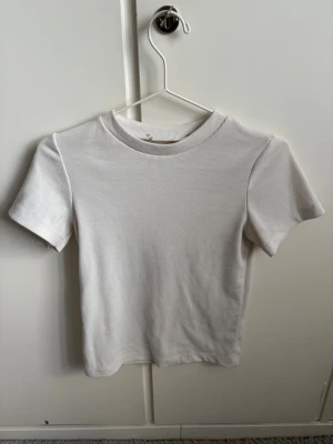 Vit ribbad t-shirt - En enkel och stilren vit t-shirt med ribbad struktur. T-shirten har korta ärmar och rund halsringning. Perfekt basplagg som passar till det mesta och är lätt att matcha med andra plagg.