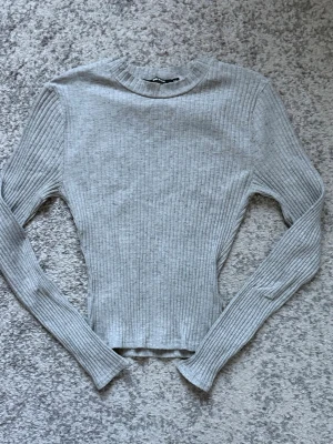 Ljusgrå ribbstickad tröja - Säljer en ljusgrå ribbstickad tröja med lång ärm och rund hals. Tröjan har en smal passform och är tillverkad i ett mjukt, stretchigt material. Perfekt basplagg för lager på lager och enkel att matcha med olika stilar.