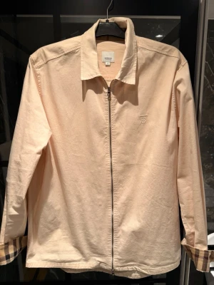 Beige overshirt från Burberry - Stilren beige overshirt från Burberry med dragkedja framtill och klassiskt rutigt foder i ärmsluten. Den är i mycket bra skick! 