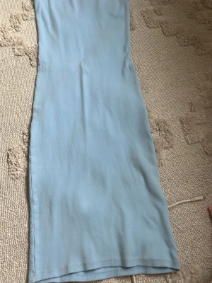 Ljusblå ribbad långklänning - Säljer en enkel och stilren ljusblå långklänning i ribbat material. Klänningen har en rak passform och är perfekt för varma dagar. Superskön och lätt att styla med accessoarer.