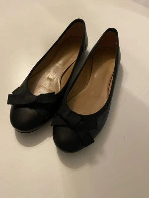 Svarta ballerinaskor från Rizzo - Klassiska svarta ballerinaskor från Rizzo med rund tå och dekorativ rosett framtill. Skorna har låg klack och en enkel, stilren design. Perfekta till jeans eller kjol för en snygg och tidlös look. Nypris ca 1800kr, strl 37!💕