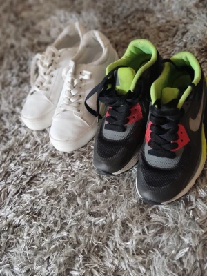 Nike Air Max sneakers svart/grå - Nike Air Max sneakers i svart och grått med detaljer i limegrönt och rött. Skorna har en klassisk siluett med synlig Air Max-sula och svarta skosnören. Tillverkade i syntetmaterial och mesh för bra andningsförmåga. Perfekta för dig som gillar sportig stil.
