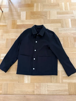 Svart overshirt Arket - Stilren svart overshirt med raka linjer, klassisk krage och stora framfickor. Storlek 46 från arket. 