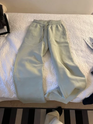 Ljusgröna mjukisbyxor med dragsko - Säljer ett par ljusgröna mjukisbyxor med bred passform och resår i midjan samt dragsko för justerbar komfort. Byxorna har raka ben och är tillverkade i ett mjukt, tjockt material som känns riktigt skönt mot huden. Perfekta för chill dagar hemma eller när du vill vara extra bekväm.