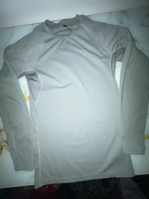 Ljusgrå långärmad topp - En enkel och stilren ljusgrå långärmad topp med rund hals. Tillverkad i ett mjukt och stretchigt material som sitter bekvämt mot kroppen. Perfekt att bära som basplagg eller under en hoodie.