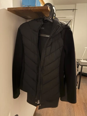 Svart pufferjacka med huva - Säljer en svart pufferjacka från Cubus med huva och dragkedja framtill. Jackan har quiltad front och släta ärmar, vilket ger en snygg och modern look. Perfekt för kalla dagar och enkel att matcha med olika outfits.