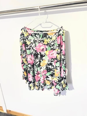 Blommig kortkjol i färgglada toner - Säljer en blommig kortkjol med svart bas och färgglada blommor i rosa, gul, grön och vit. Kjolen har en flowy passform och är perfekt för dig som gillar färg och mönster. Materialet känns lätt och luftigt.