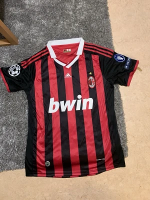 L. Riktig AC Milan från 2009/2010 - Riktig Ac Milan från 2009/2010 Den har varit köpt över 16 år sen pappa fick den av sin bror och ingen av oss syskon eller pappa mamma gillar Ac Milan därför väljer att sälja den inga skador eller fläckar en klassisk AC Milan matchtröja från Adidas med Inzaghi och nummer 9 på ryggen. Tröjan är svart och röd med vita detaljer, Champions League-märken på ärmarna och Bwin som sponsor på bröstet. Tillverkad i lätt och ventilerande material.