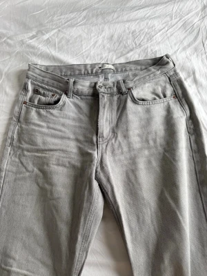 Grå raka jeans i klassisk modell - Snygga grå jeans med raka ben och fem klassiska fickor. Jeansen har bälteshällor och stängs med dragkedja och knapp. Perfekta för en avslappnad och stilren look.