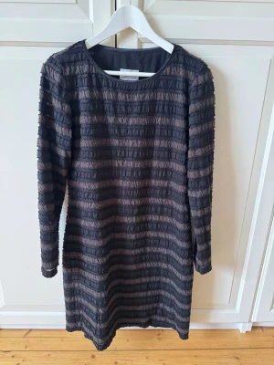 Svart långärmad klänning med struktur - Cool svart klänning från Allison med lång ärm och strukturerade horisontella ränder. Klänningen har en rund halsringning och är gjord i ett mjukt syntetmaterial. 