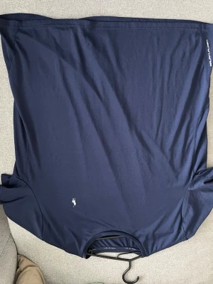 Mörkblå t-shirt från Polo Ralph Lauren träningströja - Snygg mörkblå träningströja Polo Ralph Lauren med klassisk logga broderad på bröstet. T-shirten har rund halsringning och korta ärmar. Tillverkad i mjukt material som känns skön mot huden. Perfekt till när du ska träna