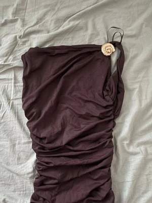 Brun open back lyx Zara klänning - Säljer en mörkbrun open back klänning med snygg rynkning och en dekorativ detalj i guld vid axelbandet. Klänningen har en tight passform och är perfekt . Materialet känns mjukt och stretchigt.