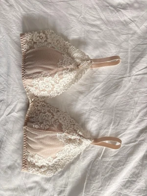 Beige spets-bh med blommönster - Söt och feminin Intermissmi liknad bh i beige/rosa med vackra vita spetsdetaljer och blommönster. Bh:n har justerbara axelband och mjuka kupor utan bygel för extra komfort. Materialet är en kombination av mesh och spets som ger en romantisk känsla. Aldrig använd bara provad!