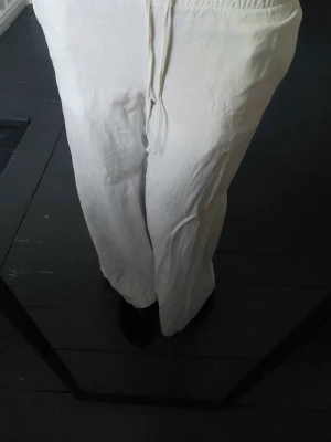 Vita linnebyxor  - Säljer ett par cremevita linnebyxor med avslappnad passform och dragsko i midjan. Byxorna har raka, vida ben och är tillverkade i ett lätt och luftigt linnetyg. Perfekta för en chill och stilren look. Köpt för 399, oanvända.