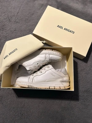 Vita sneakers från Axel Arigato - Snygga vita sneakers från Axel Arigato i läder med klassisk låg siluett. Skorna har vita snören, diskret logga på sidan och robust sula. Perfekta för dig som gillar stilrena och trendiga skor. Levereras med originalkartong och dustbag.