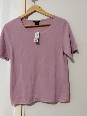 Ljuslila t-shirt från Lindex  - En enkel och stilren ljuslila t-shirt från Lindex med rund halsringning och korta ärmar. Tillverkad i mjuk bomull som känns skön mot huden. Perfekt att matcha med jeans eller kjol för en avslappnad look.